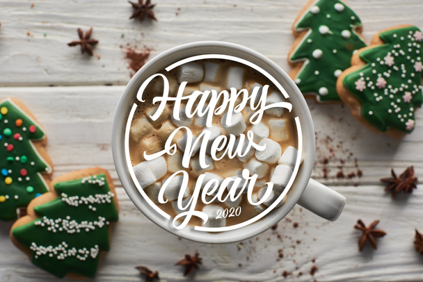 top view of Christmas cacao with marshmallow in mug on white wooden table near anise and cookies with happy new year lettering - Foto, afbeelding
