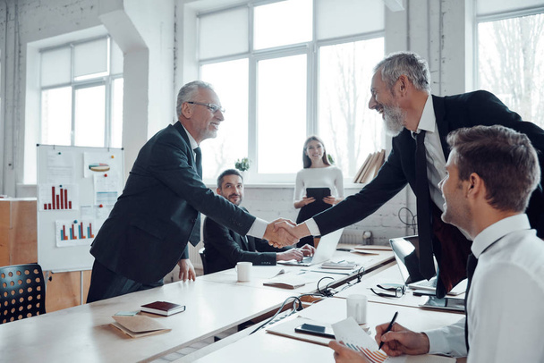 Modern businessmen shaking hands while working together with their team in the office                    - Fotoğraf, Görsel