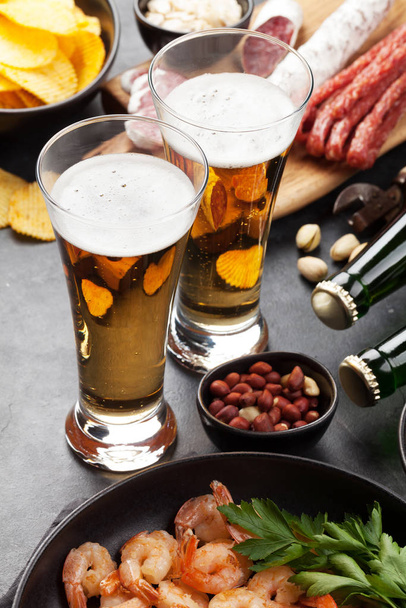 Βαρελίσια μπίρα και σνακ σε πέτρινο φόντο. Ξηροί καρποί, πατατάκια, λουκάνικα και γαρίδες - Φωτογραφία, εικόνα