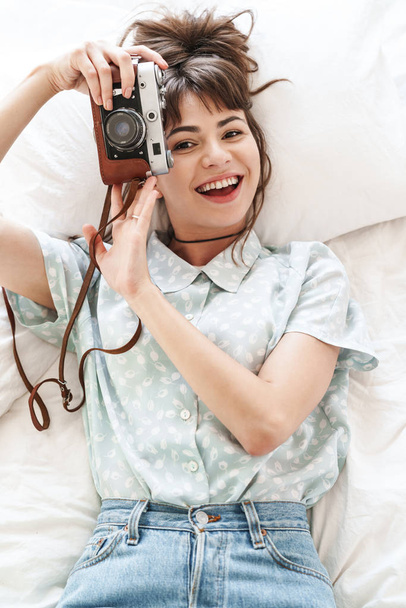 Happy cheery positive woman indoors at home lies on bed in the morning holding camera photographing. - Foto, Bild