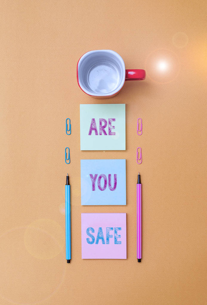 Text sign showing Are You Safe. Conceptual photo Free from danger Not anticipating any Harm Hurt physically Coffee cup blank colored sticky note two ballpoints clips yolk background. - Photo, Image