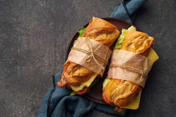Fresh big baguette sandwiches with bacon and chedder cheese and lettuce with vegetables on textile  - Fotografie, Obrázek