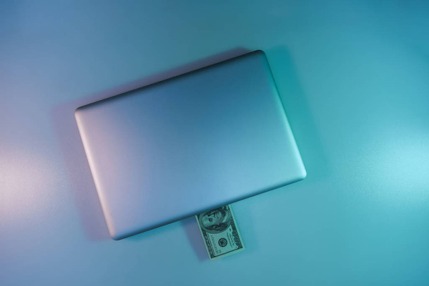 schönen silbernen Laptop und Bargeld-Dollar-Banknote in der Farbe Licht auf einem Tisch und Hintergrund. Arbeitsnachtkonzept. Ansicht von oben.  - Foto, Bild