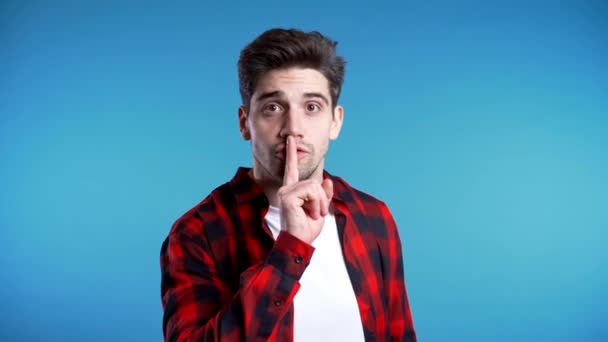 europäischer gutaussehender Mann mit dem Finger auf den Lippen vor blauem Hintergrund. Geste von shhh, Geheimnis, Schweigen - Filmmaterial, Video