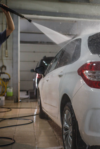 The car is hand-washed. The washer washes the car from the high-pressure apparatus and wipes the glass. - Foto, Imagen