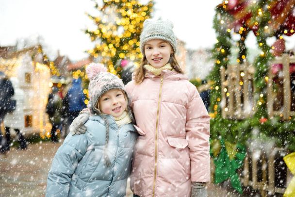 Two adorable sisters having a good time together on traditional Christmas fair in Riga, Latvia. Children enjoying sweets, candies and gingerbread on Xmas market. Winter time with family and kids. - Photo, Image