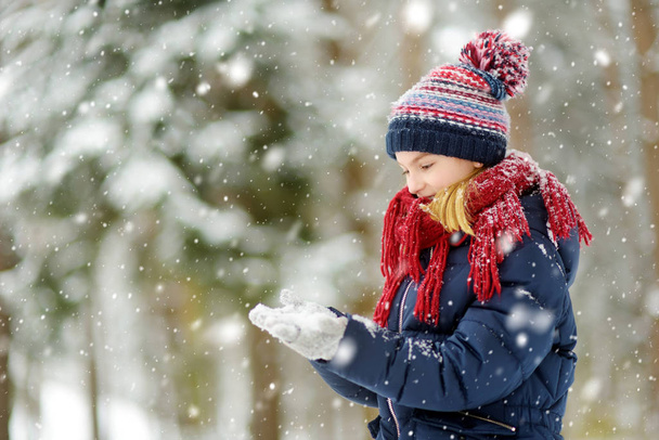 Adorable young girl having fun in beautiful winter park during snowfall. Cute child playing in a snow. Winter activities for family with kids. - Φωτογραφία, εικόνα