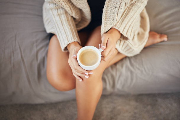 Вид зверху біла жінка, одягнена в бежевий светр, сидить на ліжку і тримає каву
. - Фото, зображення