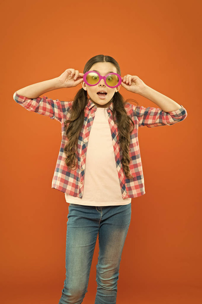Aint it funny. Little girl looking through funny glasses with color filter on orange background. Funny child wearing sunglasses on surprised face. My eyes go funny - Foto, imagen