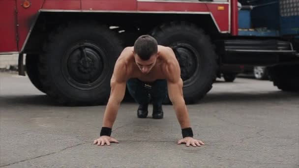 Przystojny młody sportowiec robi pompki z klaskaniem na zewnątrz z wozem strażackim w tle - Materiał filmowy, wideo