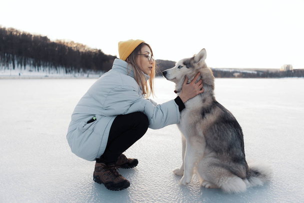 Happy young girl playing with siberian husky dog in winter park - Photo, Image