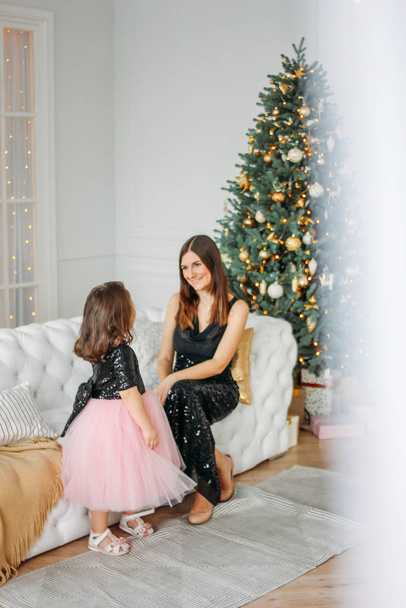 若いです母と娘で夜のドレスにクリスマスツリーを背景に - 写真・画像