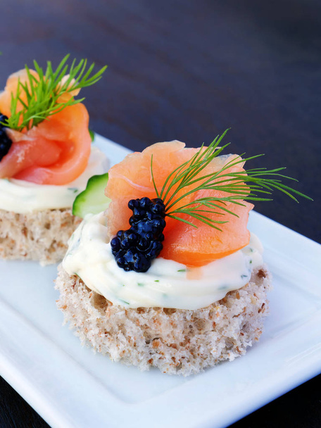 Comida para dedos con salmón ahumado y caviar en bandeja blanca sobre fondo oscuro
 - Foto, imagen