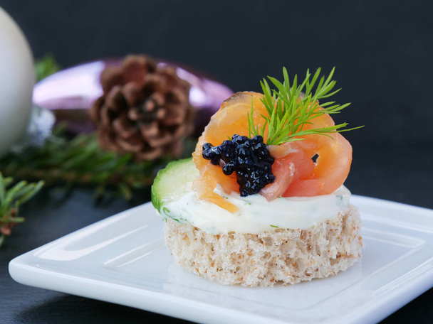 Sabrosa comida para los dedos con salmón ahumado y caviar sobre bandeja blanca sobre fondo oscuro
 - Foto, Imagen