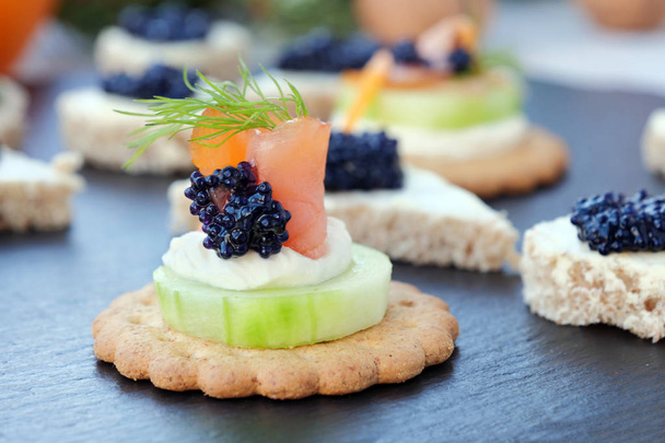 Buffet de festa sortidas, comida dedo com com salmão defumado e caviar sobre prato de ardósia preta
 - Foto, Imagem