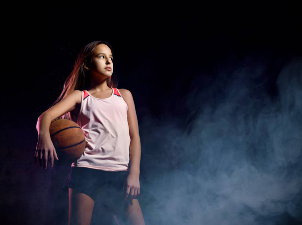 Beautiful caucasian teen woman in sportswear playing basketball . Sport concept isolated on black background. - Fotoğraf, Görsel