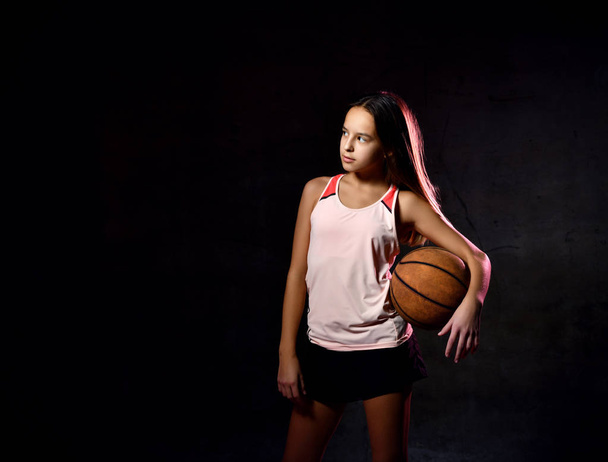 Beautiful caucasian teen woman in sportswear playing basketball . Sport concept isolated on black background. - Fotoğraf, Görsel