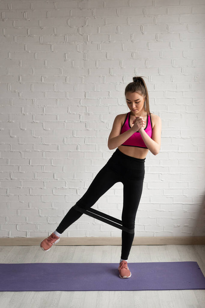An athlete in top and leggings performs exercises for the leg muscles with a fitness elastic band. - Zdjęcie, obraz
