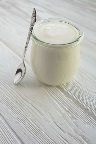 Натуральний молочний йогурт у скляній банці на білому дерев'яному фоні. Розташування вертикальне. Копіювати простір
. - Фото, зображення