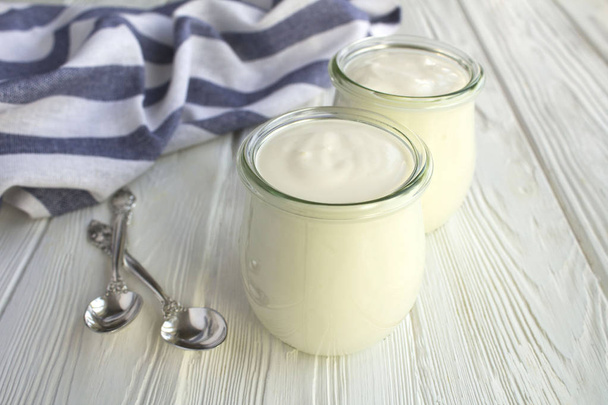Natural milk yogurt in the glass jars on the white wooden background. Closeup. - Foto, Bild