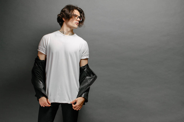 Hipster guapo modelo masculino con gafas en blanco camiseta en blanco y vaqueros negros con espacio para su logotipo o diseño en estilo urbano casual - Foto, imagen