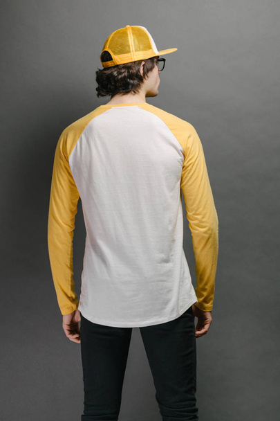 Man model with beard wearing white and yellow blank Long Sleeve Shirt for mock up and a baseball cap with space for your logo or design over gray background - Fotografie, Obrázek