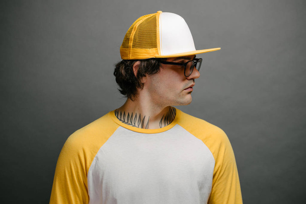 Hipster handsome male model wearing yellow blank baseball cap with space for your logo over gray background - Foto, Imagem