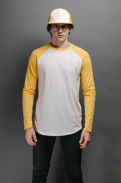 Man model with beard wearing white and yellow blank Long Sleeve Shirt for mock up and a baseball cap with space for your logo or design over gray background - Foto, imagen