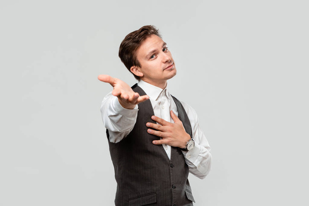 Молодой человек в белой рубашке и сером жилете делает предложение о браке изолированным на сером фоне
 - Фото, изображение
