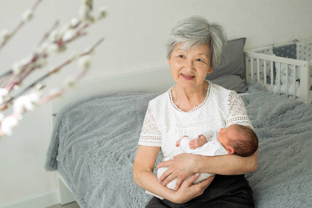 Büyük büyükannem yeni doğmuş büyük torunuyla oynuyor. Bebek büyükannenin kollarında yatıyor. - Fotoğraf, Görsel