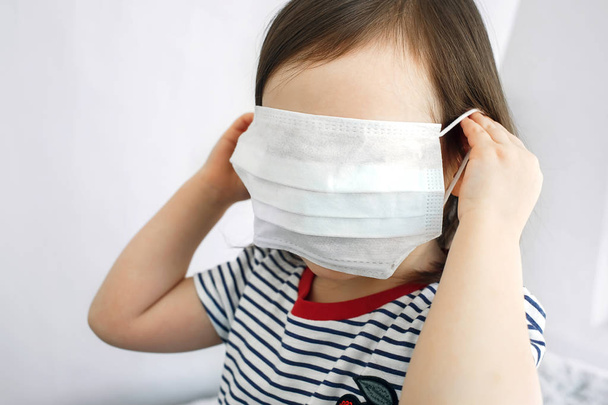 Un niño con una máscara protectora. El niño se esconde detrás de una máscara médica.
. - Foto, Imagen