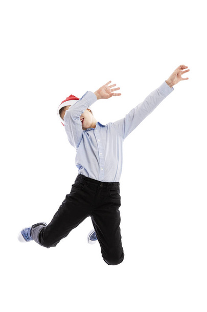 Smiling jumping schoolboy in Santa's hat. Full height. Christmas mood. Isolated over white background. Vertical. - Foto, imagen