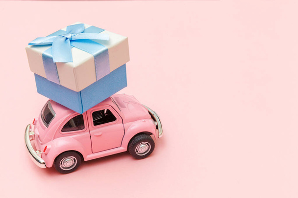 Simply design pink vintage retro toy car delivering gift box on roof isolated on trendy pastel pink background. Christmas New Year birthday Valentine's day celebration present romantic concept - Fotó, kép
