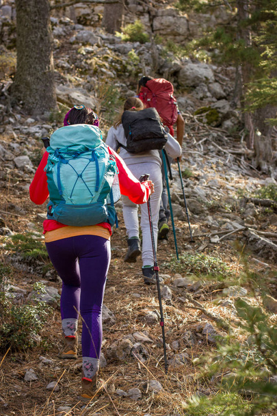 Mountain climbing. Three people go uphill with trekking poles and backpacks. - Photo, Image