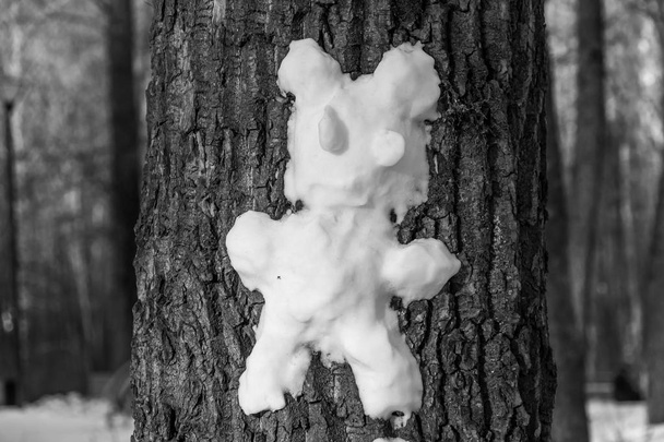 Один маленький грустный тающий снежный зверь из снега на серой коре дерева в парке
 - Фото, изображение