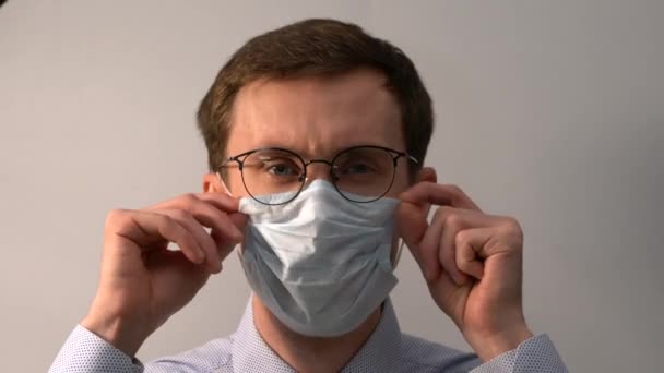 Portrait of a young man in glasses straightens a medical mask. - Video, Çekim