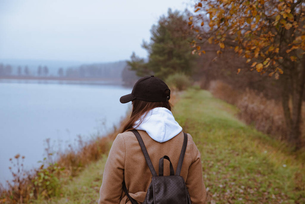 woman walking by lake coastline in autumn outfit - Photo, Image