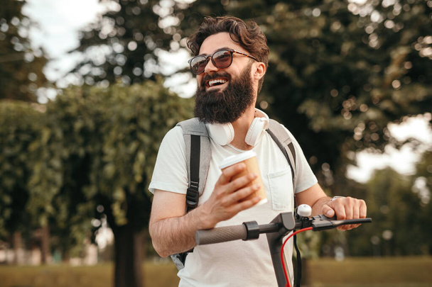 Happy hipster with drink riding scooter - Fotoğraf, Görsel
