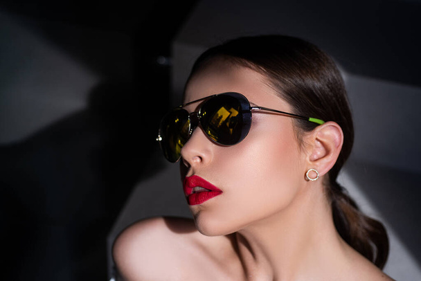 Elegant chic female model in fashion sunglasses with red lips. Portrait of serious woman in the dark isolated. Young woman posing. Portrait of a young woman in sunglasses. - Foto, afbeelding