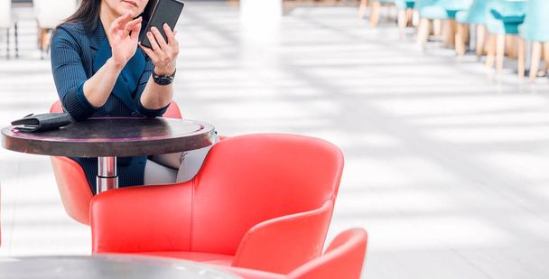 Mujer de negocios en una chaqueta azul se sienta en un centro comercial o centro de negocios en un café con sillas rojas y utiliza el teléfono
 - Foto, Imagen