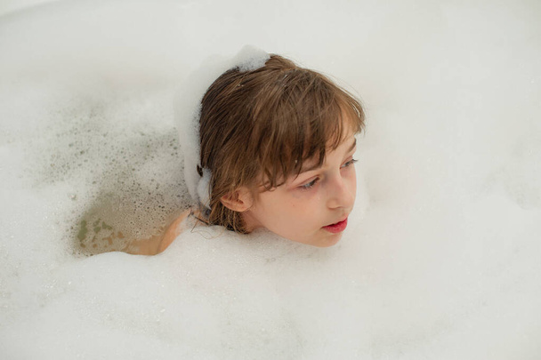 Young girl inside the bath. A little girl bathes in a bathtub with foam. - Photo, Image
