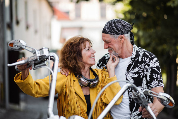 A cheerful senior couple travellers in love with motorbike in town. - Fotoğraf, Görsel