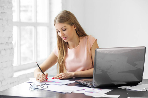 Νεαρή ενήλικη γυναίκα γράφει στο γραφείο. Η έννοια της επιχείρησης, την εργασία και τα χρήματα. - Φωτογραφία, εικόνα