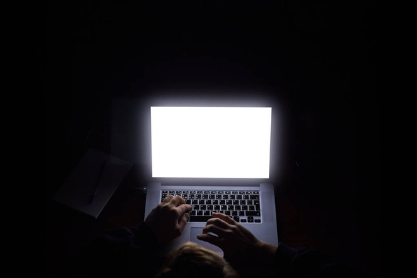 yläpuolella hakkeri konepellin kanssa kannettavan tietokoneen ja matkapuhelimen kirjoittamalla tekstiä pimeässä huoneessa
 - Valokuva, kuva