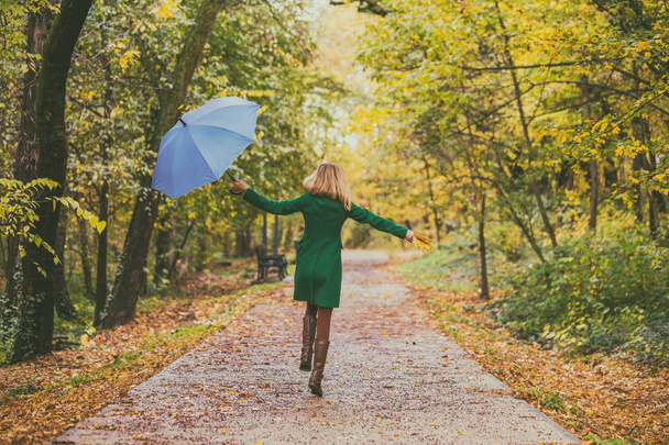 Woman holding umbrella and fall leafs while jumping and  walking in the park. - Fotografie, Obrázek