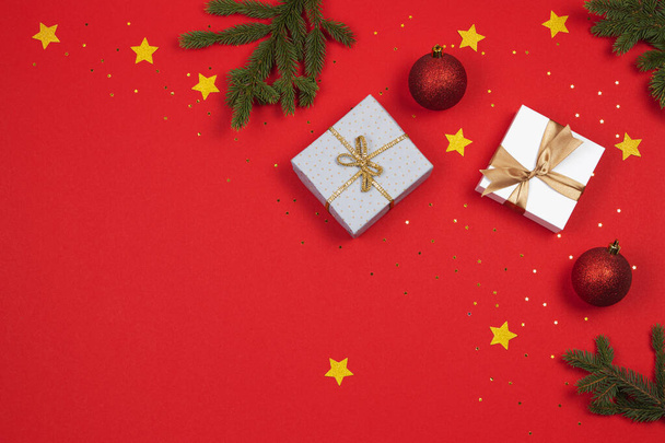 Fundo de Natal. Ramos de abeto verde, caixas de presente, bolas de bugiganga de decoração e estrelas de brilho dourado no fundo vermelho
 - Foto, Imagem