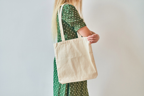 Ένα κορίτσι κρατά λευκή βαμβακερή οικολογική τσάντα, σχέδιο mockup. - Φωτογραφία, εικόνα