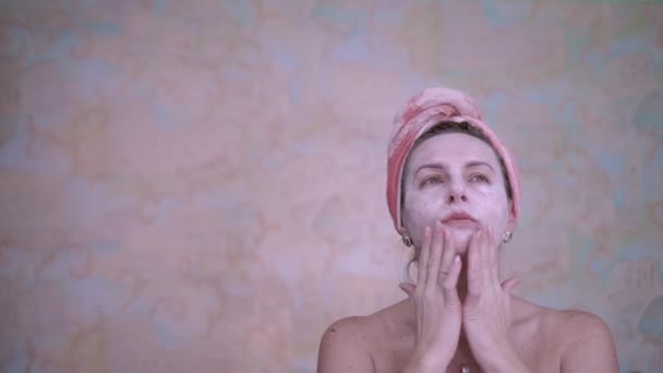 A woman with a towel on her head applied a cosmetic mask to rejuvenate and smooth wrinkles. Spa treatments. Fight against wrinkles and skin aging. - Materiaali, video