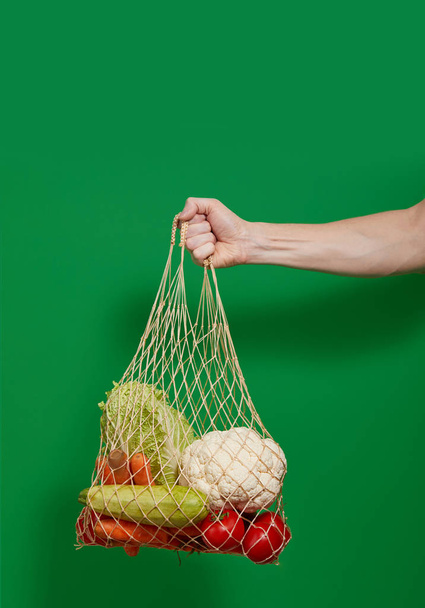 Hand holds Reusable shopping string bag with groceries on green isolated background. Zero waste concept. No plastic. - Photo, Image