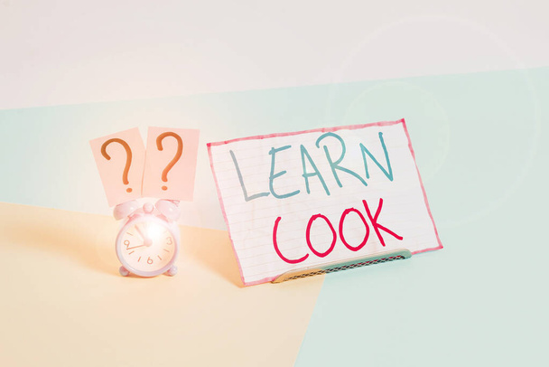 Handwriting text Learn Cook. Concept meaning gaining knowledge or acquiring skills in culinary or food Mini size alarm clock beside a Paper sheet placed tilted on pastel backdrop. - 写真・画像